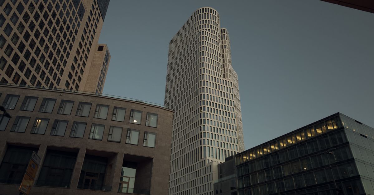 A wide-angle cinematic view of a modern European city center with people using smartphones, soft daylight, glass office buildings in the background, no visible writing or sign, calm documentary atmosphere