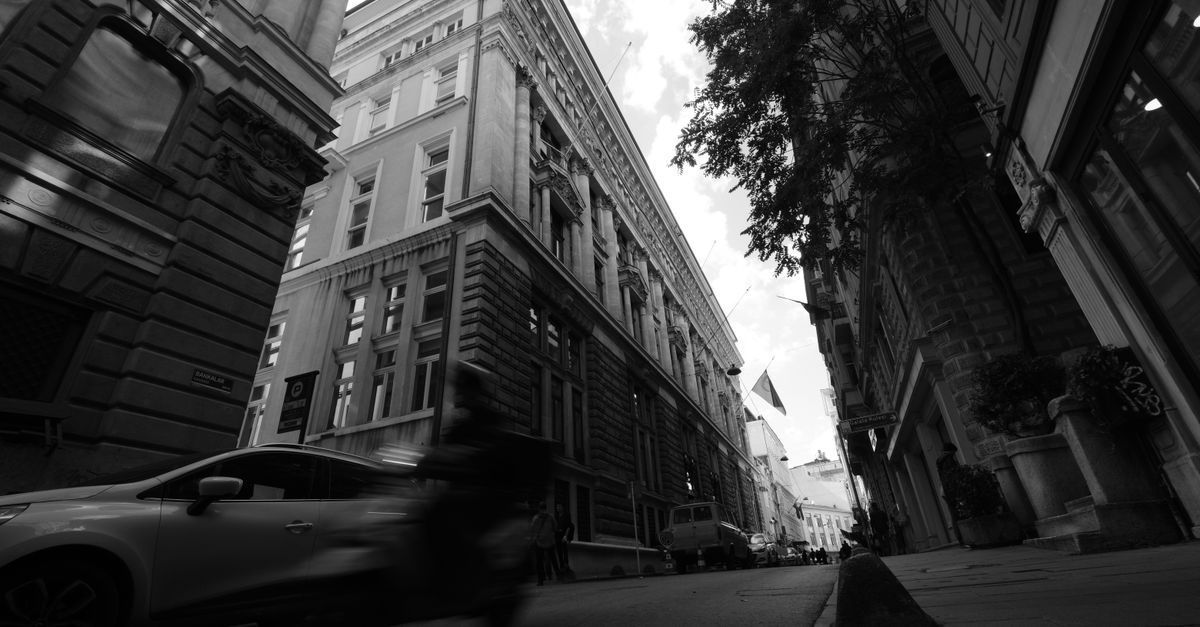 A wide-angle view of a modern European city street with people walking and holding smartphones, soft daylight, clean architecture, cinematic depth of field, no visible writing or sign, documentary style