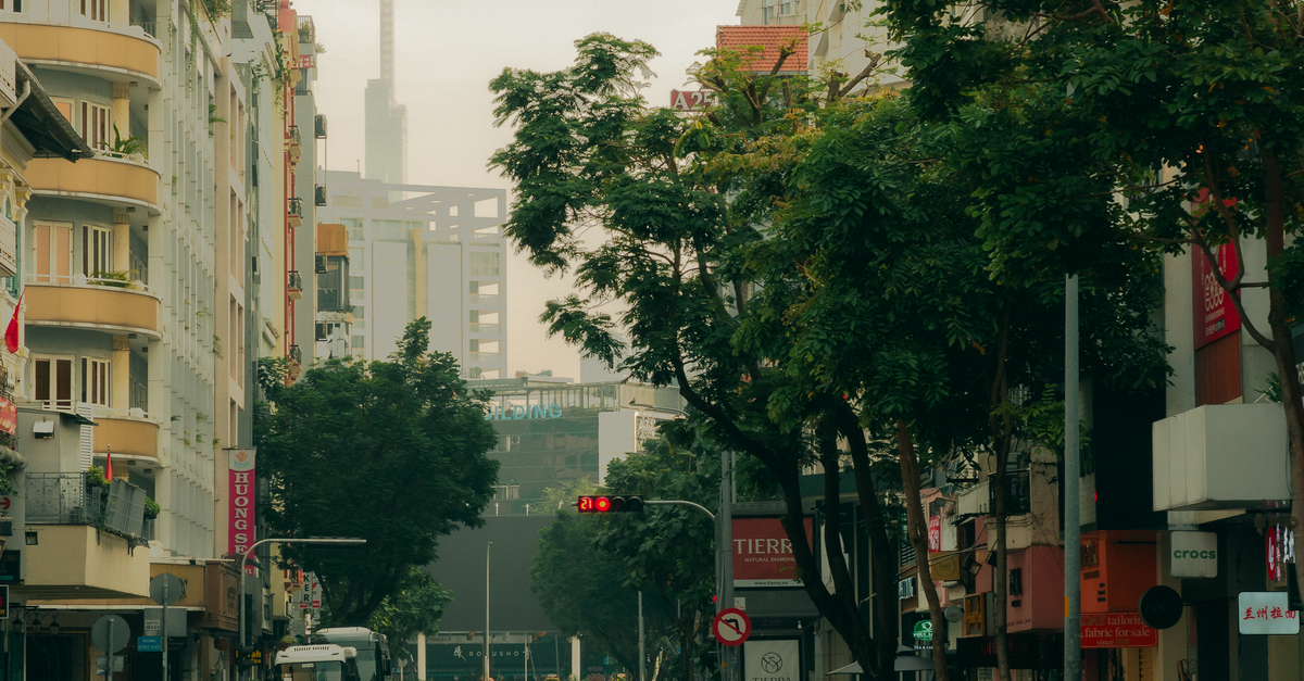 A wide street-level view of a Vietnamese urban financial district, modern bank branch exterior with glass facade, motorbikes passing in the foreground, soft afternoon light, no visible detail or sign, cinematic documentary style