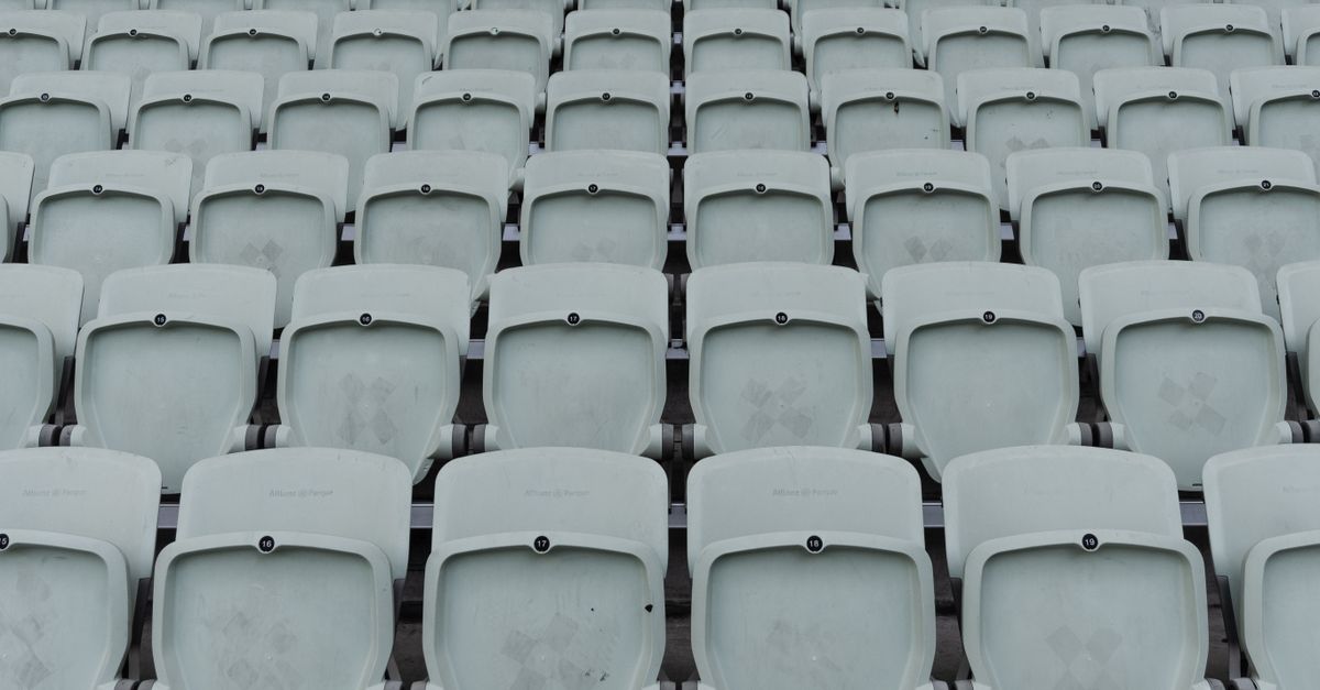 A cinematic wide-angle shot of an empty American college football stadium at dusk, modern digital billboards glowing softly without any visible detail or logos, capturing the massive scale and business atmosphere of collegiate sports, photorealistic, 8k resolution, dramatic lighting.