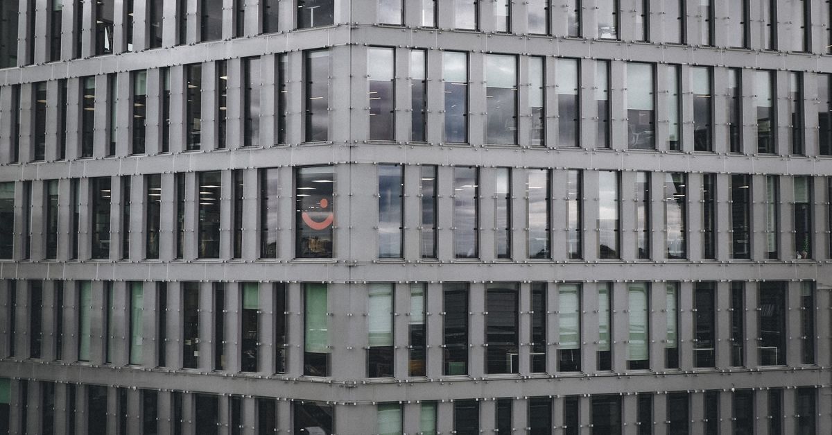 A wide-angle view of a modern glass office district in a European capital at dusk, blurred pedestrians, cinematic soft lighting, no visible writing or sign, calm analytical mood