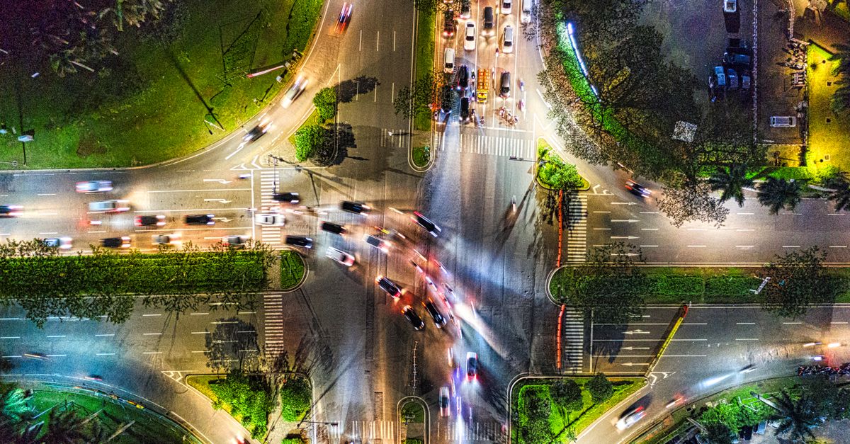 A wide-angle view of a busy Southeast Asian city street in Kuala Lumpur at dusk, warm streetlights, delivery motorbikes and parcel boxes, modern skyline in the background, cinematic lighting, no visible writing or sign