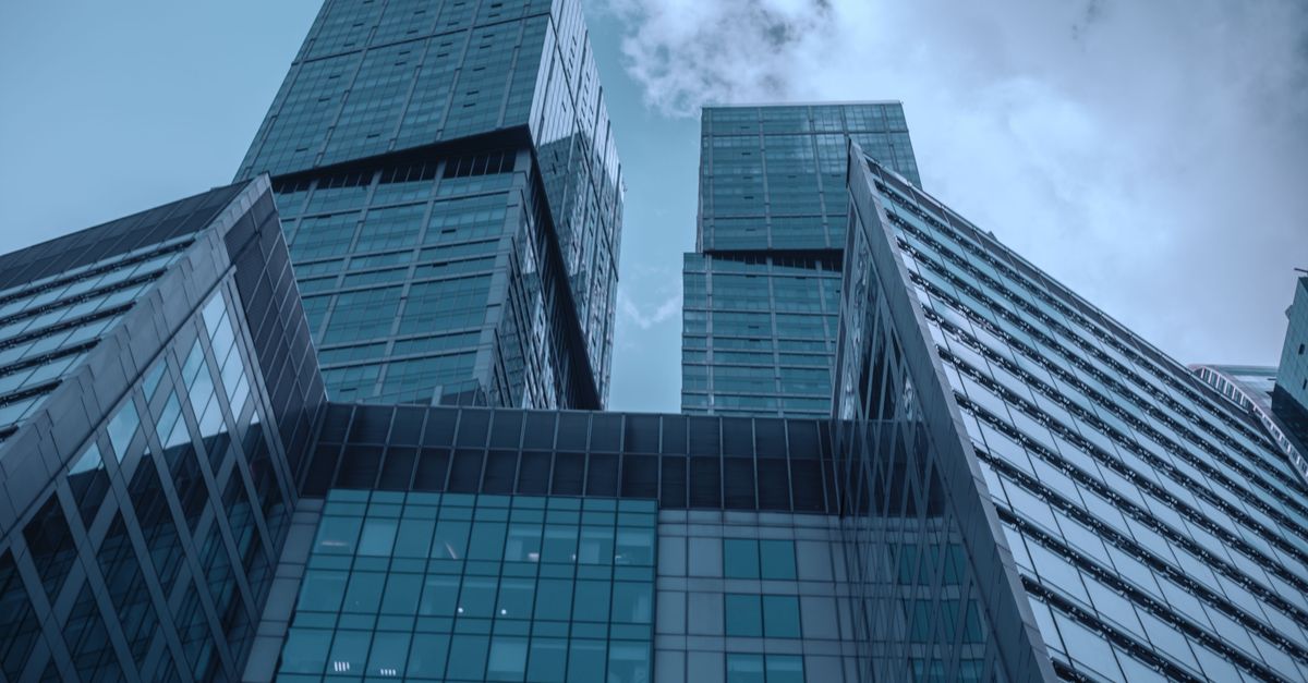 A wide-angle view of a modern financial district with glass office towers reflecting afternoon light, busy pedestrians on the street below, no visible writing on any surface, cinematic depth of field, documentary photography style