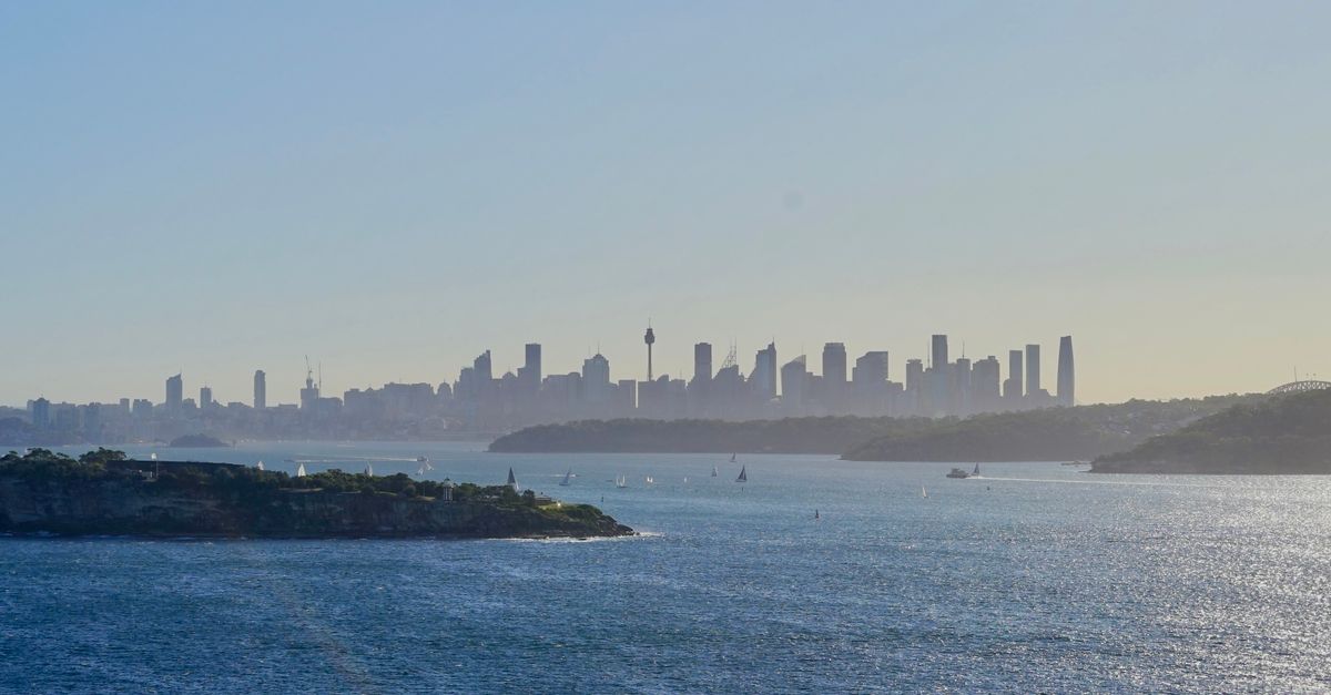 A wide-angle cityscape blending a modern Tokyo skyline and a Sydney harbor skyline under soft daylight, cool blue tones, cinematic depth, no visible writing or sign, calm professional atmosphere symbolizing international cooperation
